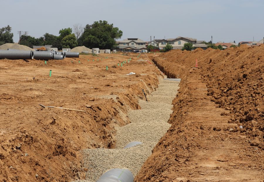 Open trench with a gravel bed and stacked pipe on a subdivision jobsite